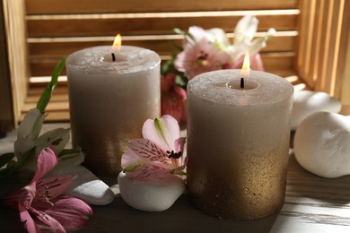 Photo of Burning candles, stones and lily flowers on wooden table, closeup