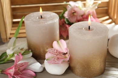 Photo of Burning candles, stones and lily flowers on wooden table, closeup