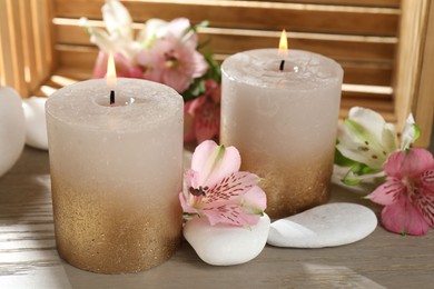 Photo of Burning candles, stones and lily flowers on wooden table, closeup