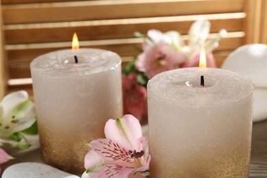 Photo of Burning candles, stones and lily flowers on wooden table, closeup