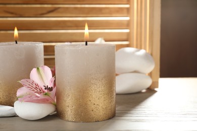 Photo of Burning candles, stones and lily flowers on wooden table, closeup