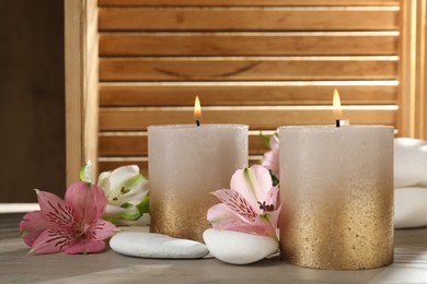 Photo of Burning candles, stones and lily flowers on wooden table, closeup