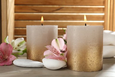 Photo of Burning candles, stones and lily flowers on wooden table, closeup