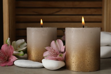 Photo of Burning candles, stones and lily flowers on wooden table, closeup