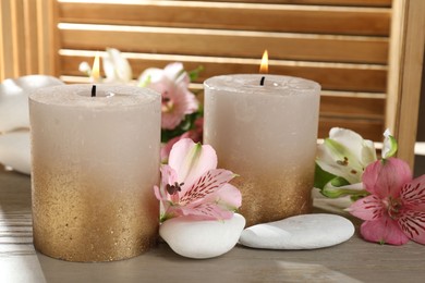 Photo of Burning candles, stones and lily flowers on wooden table, closeup
