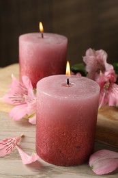 Photo of Burning candles and lily flowers on white wooden table, closeup