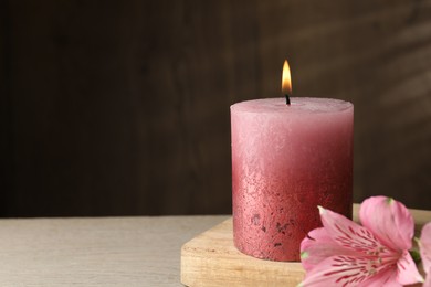 Photo of Burning candle and lily flowers on table, closeup. Space for text