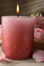 Photo of Burning candle and lily flowers on white wooden table, closeup