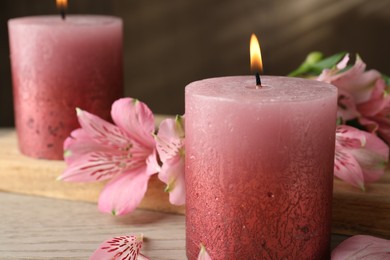 Photo of Burning candles and lily flowers on white wooden table, closeup
