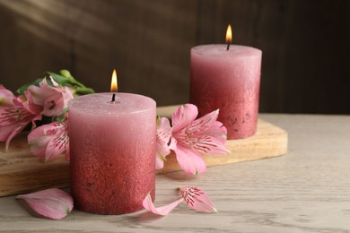 Photo of Burning candles and lily flowers on white wooden table, closeup