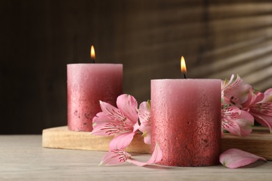 Photo of Burning candles and lily flowers on white wooden table, closeup