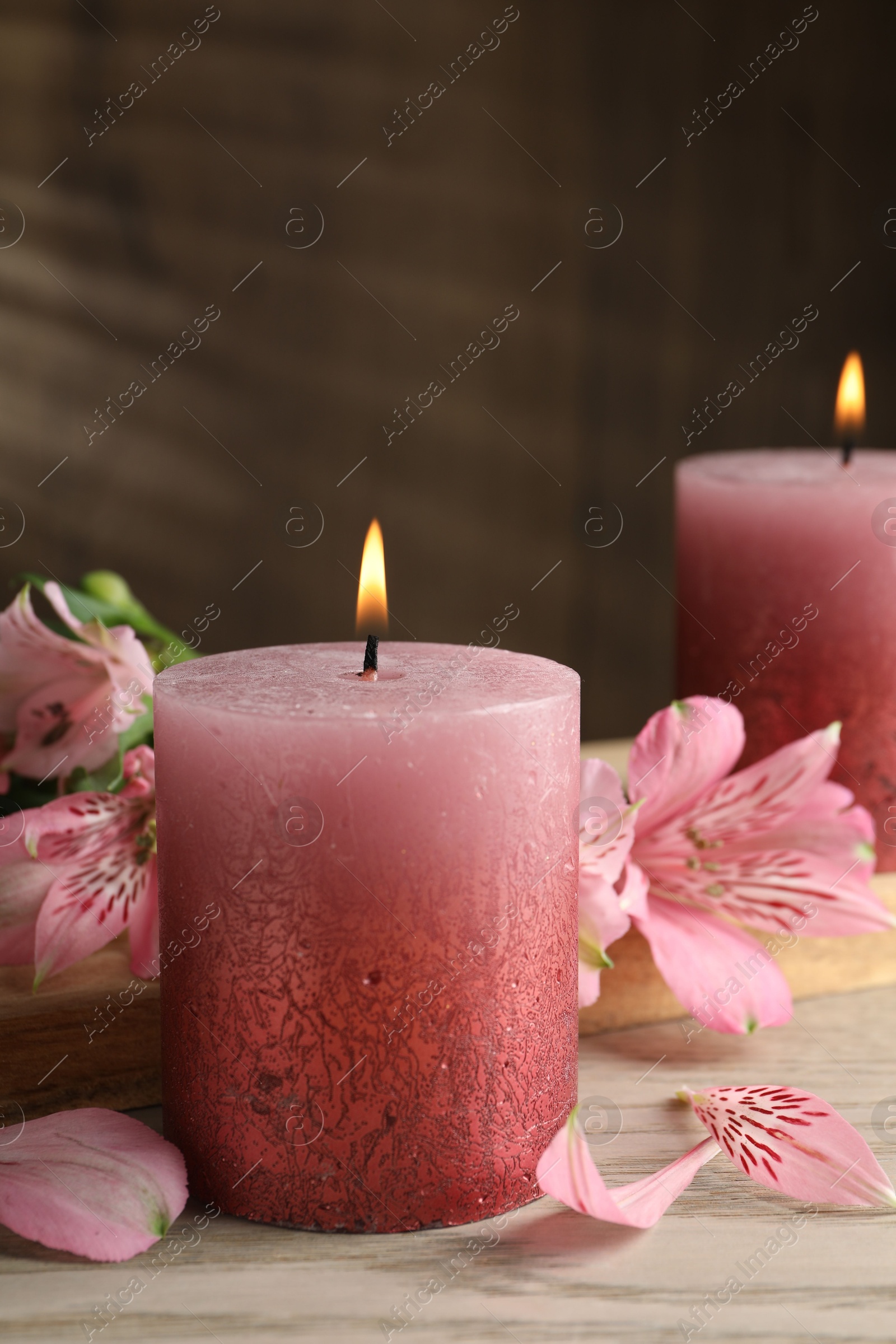 Photo of Burning candles and lily flowers on white wooden table, closeup