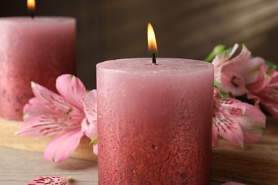 Photo of Burning candles and lily flowers on white wooden table, closeup