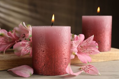 Photo of Burning candles and lily flowers on white wooden table, closeup
