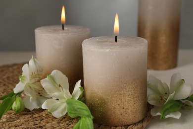 Photo of Burning candles and lily flowers on white table, closeup
