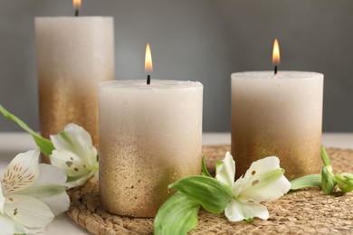 Photo of Burning candles and lily flowers on white table, closeup
