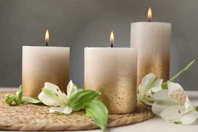 Photo of Burning candles and lily flowers on white table, closeup