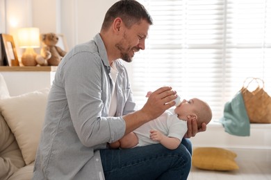 Photo of Father feeding his little baby with bottle on sofa at home