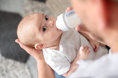Photo of Father feeding his little baby with bottle at home, closeup