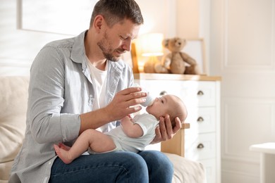 Photo of Father feeding his little baby with bottle on sofa at home