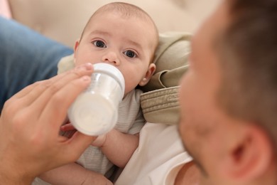 Photo of Father feeding his little baby with bottle on sofa at home, closeup