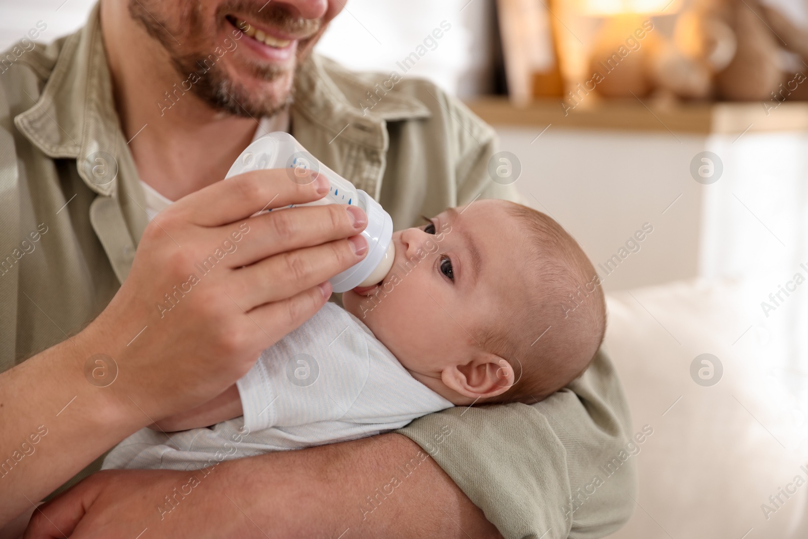 Father feeding his little baby with bottle on sofa at home, closeup Photo of Father feeding his little baby with bottle on sofa at home, closeup