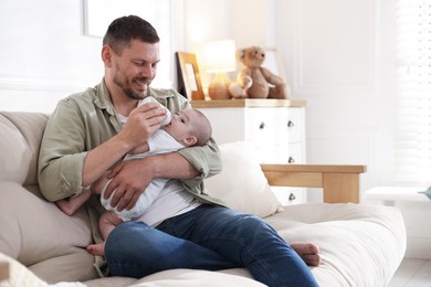 Photo of Father feeding his little baby with bottle on sofa at home. Space for text