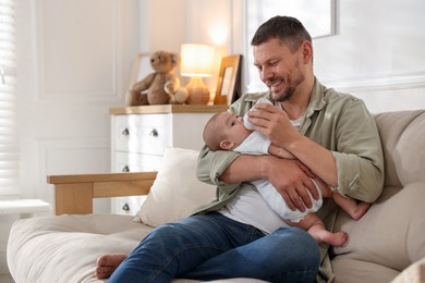 Photo of Father feeding his little baby with bottle on sofa at home. Space for text