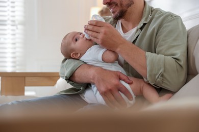 Photo of Father feeding his little baby with bottle on sofa at home, closeup