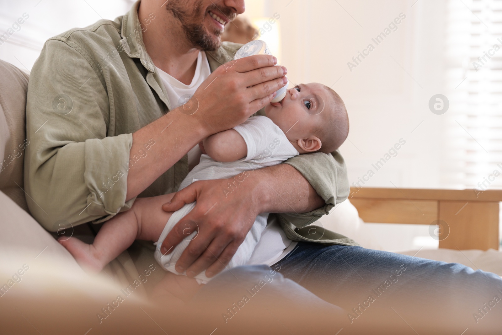 Father feeding his little baby with bottle on sofa at home, closeup Photo of Father feeding his little baby with bottle on sofa at home, closeup