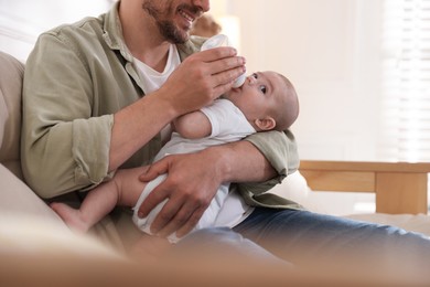 Photo of Father feeding his little baby with bottle on sofa at home, closeup