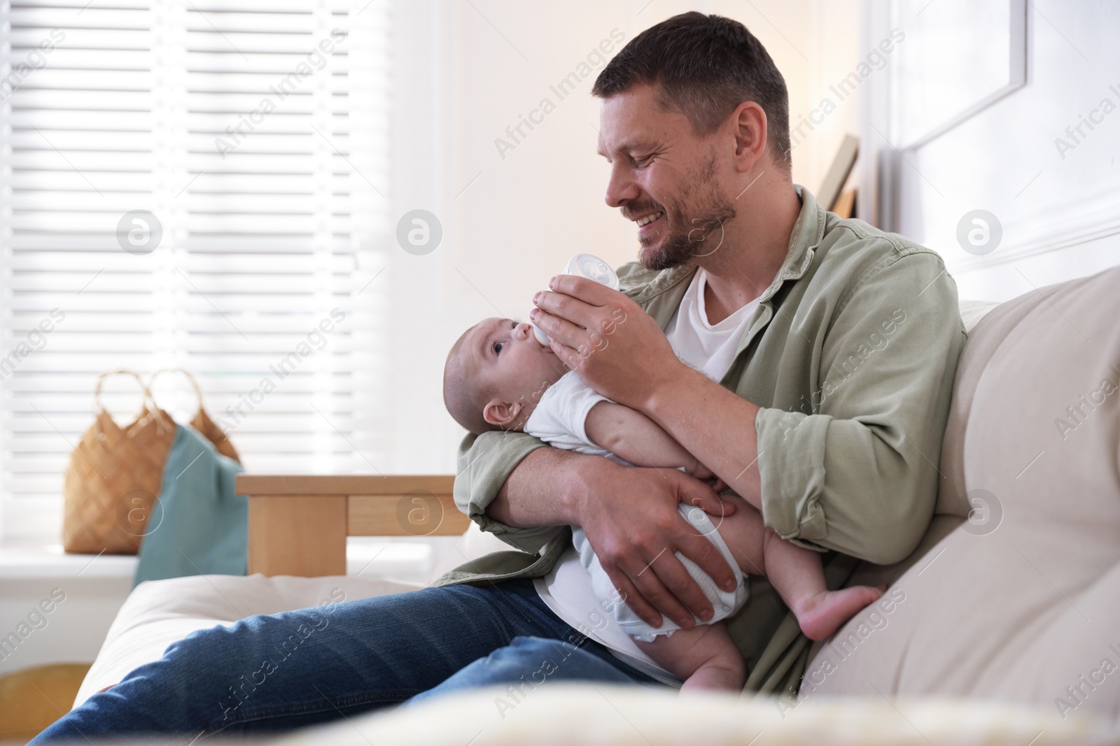 Father feeding his little baby with bottle on sofa at home. Space for text Photo of Father feeding his little baby with bottle on sofa at home. Space for text