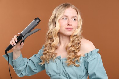 Photo of Woman with beautiful hair and curling iron on brown background