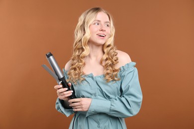Photo of Woman with beautiful hair and curling iron on brown background