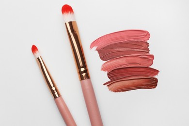Photo of Colorful lip glosses and makeup brushes on grey background, flat lay