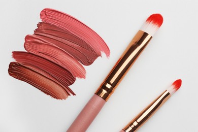 Photo of Colorful lip glosses and makeup brushes on grey background, flat lay