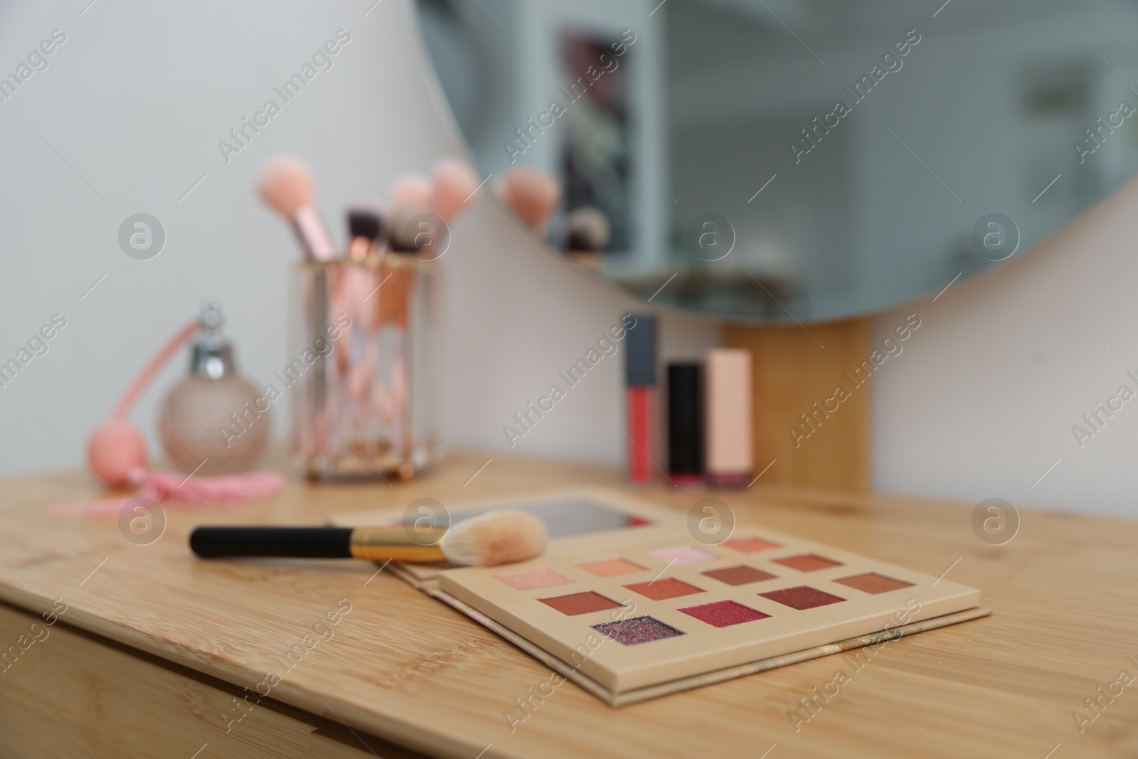 Eyeshadow palette with brush on wooden dressing table indoors, closeup. Cosmetic products Photo of Eyeshadow palette with brush on wooden dressing table indoors, closeup. Cosmetic products