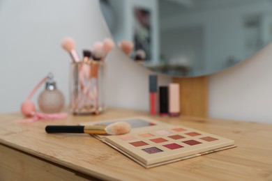 Photo of Eyeshadow palette with brush on wooden dressing table indoors, closeup. Cosmetic products