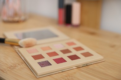 Photo of Eyeshadow palette with brush on wooden dressing table indoors, closeup. Cosmetic products
