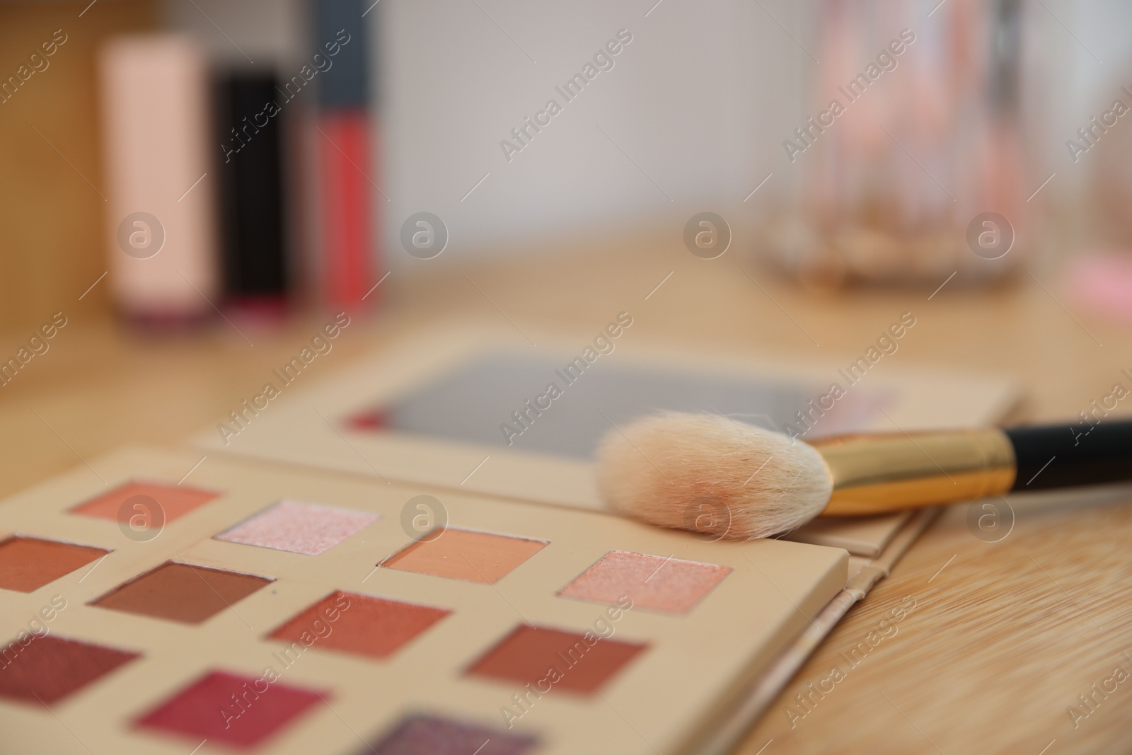 Eyeshadow palette with brush on wooden dressing table indoors, closeup. Cosmetic products Photo of Eyeshadow palette with brush on wooden dressing table indoors, closeup. Cosmetic products