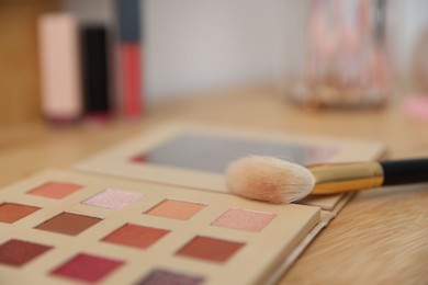 Photo of Eyeshadow palette with brush on wooden dressing table indoors, closeup. Cosmetic products