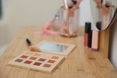 Photo of Eyeshadow palette with brush on wooden dressing table indoors, closeup. Cosmetic products