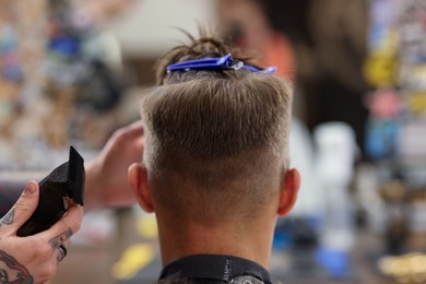 Photo of Professional barber making stylish haircut in barbershop, closeup