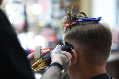 Photo of Professional barber making stylish haircut in barbershop, closeup