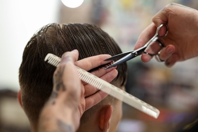 Photo of Professional barber cutting client's hair with scissors in barbershop, closeup