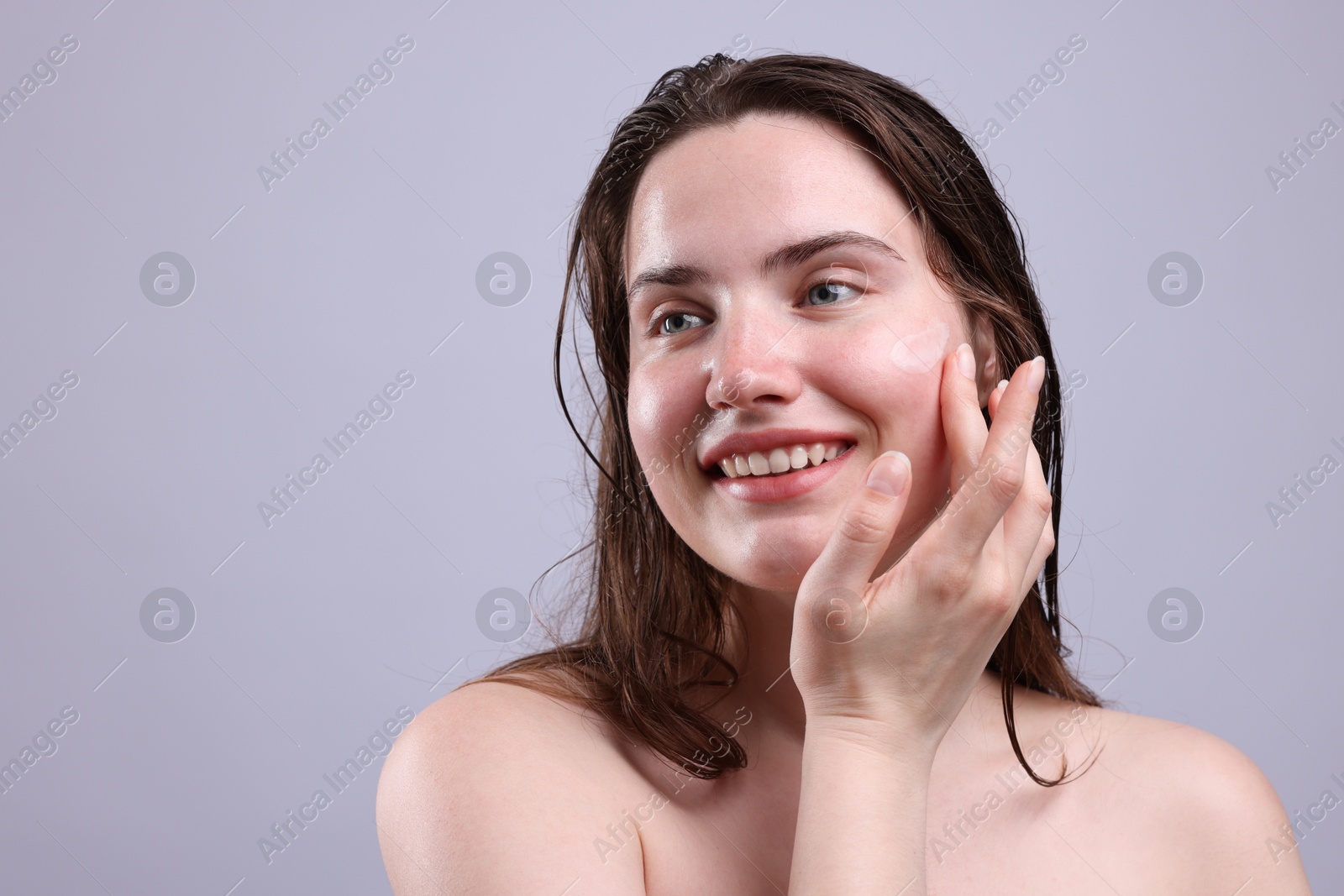Smiling woman applying skincare product onto her face on grey background, closeup. Space for text Photo of Smiling woman applying skincare product onto her face on grey background, closeup. Space for text