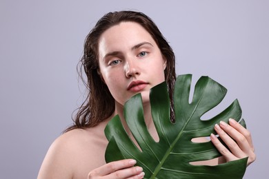 Photo of Portrait of beautiful woman with natural skin complexion holding monstera leaf on grey background, closeup