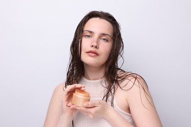Photo of Portrait of beautiful woman with jar of skincare product on light grey background, closeup