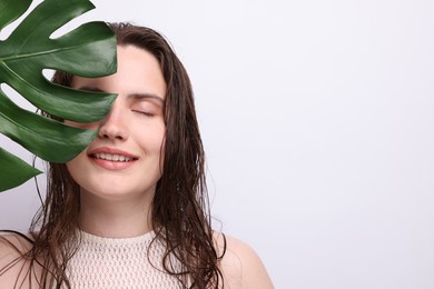 Photo of Portrait of smiling woman with natural skin complexion and monstera leaf on grey background, closeup. Space for text