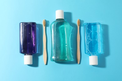 Photo of Bottles of mouthwash and toothbrushes on light blue background, flat lay